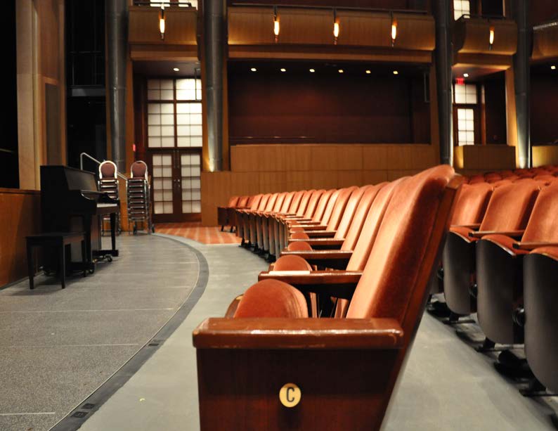 Rows of empty theater seats facing a stage area in an auditorium.